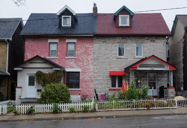 two attached houses in the Junction, one painted red brick with dark blue roof and the other light brown with dark red roof and bright red trim, small white picket fence in front of the red house, metal fence in front of the brown house (beige actually) 