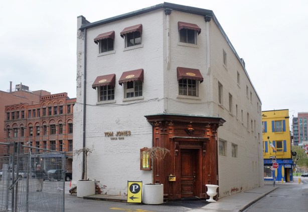 Tom Jones restaurant, three storey white brick building, stand alone, parking lot on one side, street on the other, dark wood door and door frame, 