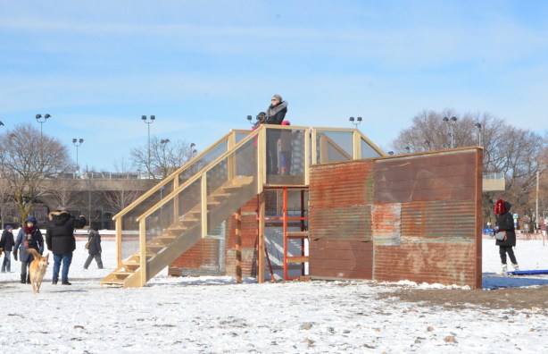 two wooden staircases meet at the top, above an old rusty corrugated metal wall, platform at the top for people to meet