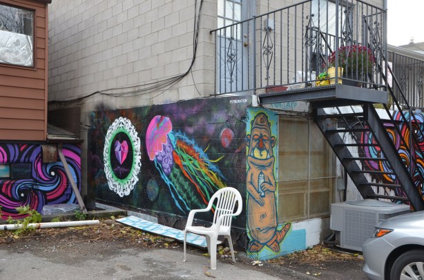 white plastic chair outside in alley in front of a mural of a jellyfish and a heart 