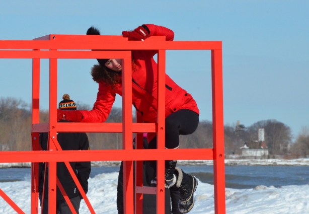 a woman in a red parka is climbing onto an elevated red metal seat