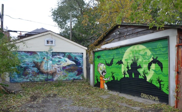 two murals on garage doors in Feel Good Lane, one a green halloween-like scene with silhouettes of bats the other is a marine scene 