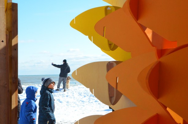 part of 'Forest of Butterflies' sculpture in the foreground, along with two boys who are looking at it In the background, standing on a hill of snow, is a man taking a selfie with his golden lab dog 