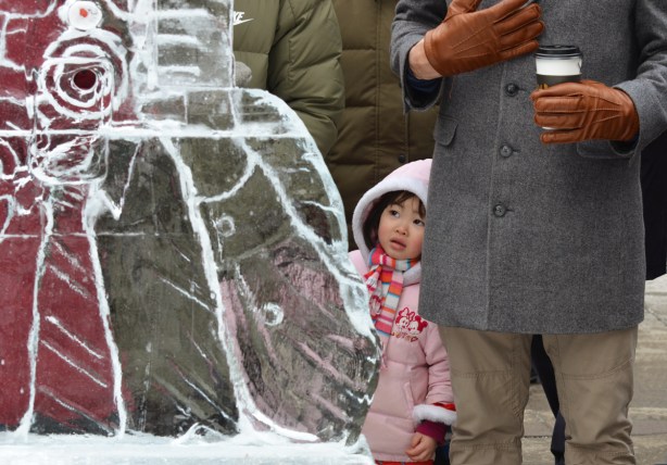 a little girl in pink looks out from behind a man an ice sculpture