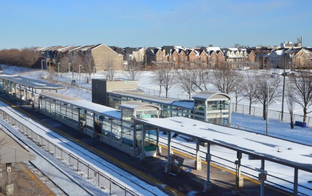 view from a bridge over railway tracks, Danforth GO station below, houses beyond. covered platforms between two sets of tracks 