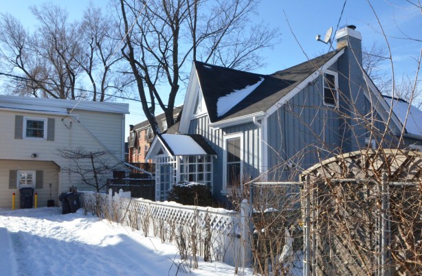 a workers cottage that fronts onto a snow covered lane, grey vertical wood paneling on the outside, black roof 