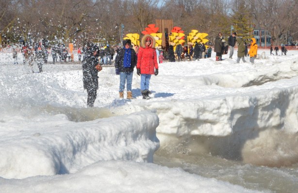 standing on the snow and ice covered beach in February, wavy day, waves crashing against shore producing spray , people standing and watching 