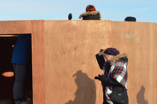 a woman in a tartan scarf walks past 'Mind Station', an art installation at Woodbine Beach made of plywood