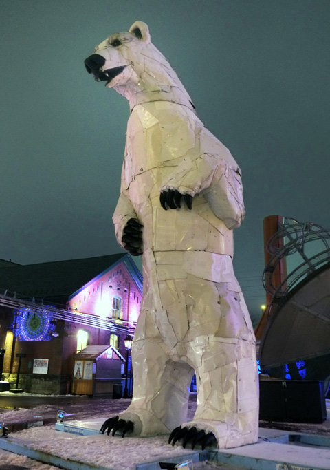 a sculpture of a very large polar bear standing on its hind feet, in white, with black claws and facial features, distillery district, evening
