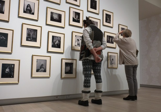 Two women are looking at a wall covered with framed black and white photos at the Ryerson Image Centre