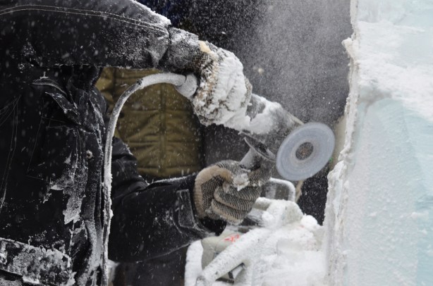 using a power sander, a man is creating a sculpture out of a block of ice