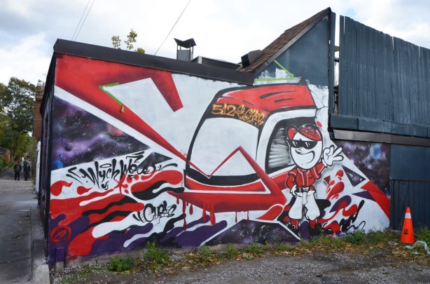 red and white mural of a man (cartoon like) beside a TTC 512 St. Clair street car, in Feel Good Lane 