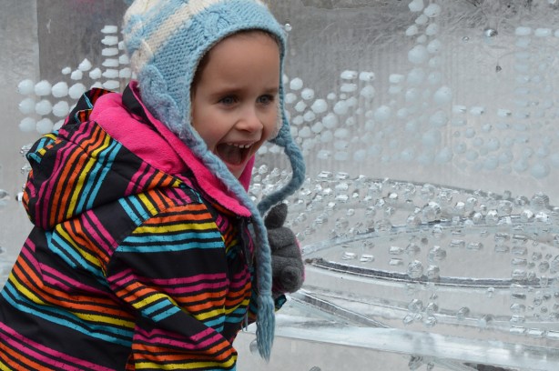 a child ina striped jacket and mouth open wide poses beside an ice sculpture