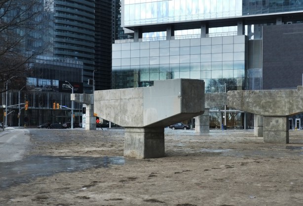 four or five concrete bents stand in a vacant piece of land tht is being made into a park. the bents once held up an off ramp of the Gardiner Expressway
