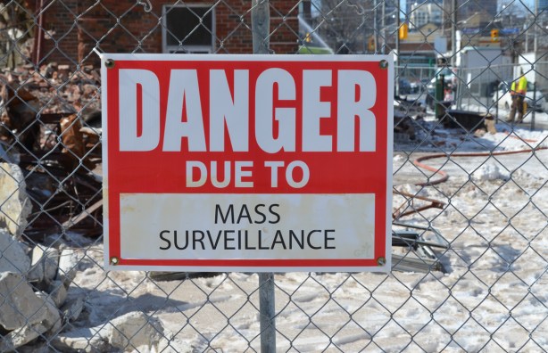 red and white sign, danger due to signs, on a chainlink fence at a construction site in Regent Park, danger due to mass surveillance