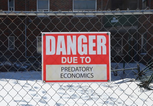 red and white sign, danger due to signs, on a chainlink fence at a construction site in Regent Park, danger due to predatory economics
