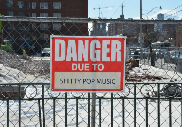 red and white sign, danger due to signs, on a chainlink fence at a construction site in Regent Park, danger due to shitty pop music