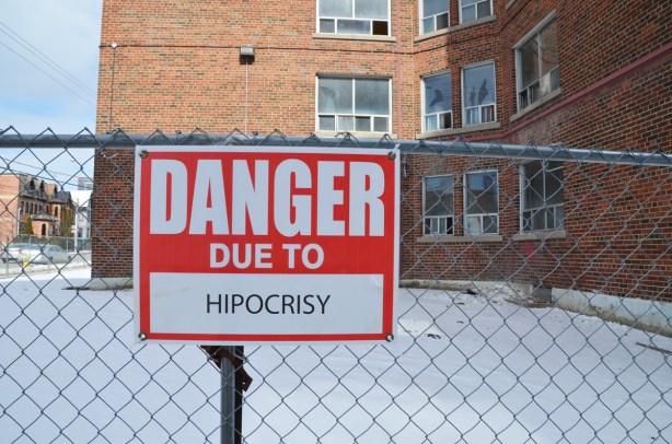 red and white sign, danger due to signs, on a chainlink fence at a construction site in Regent Park, danger due to hypocrisy (but spelled as hipocrisy)