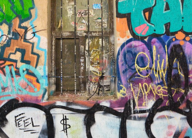 an old window with stickers on it and rusted bars in front of it, graffiti all around it 