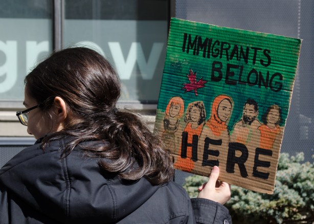 a woman holds a small painted sign that says immigrants belong here 