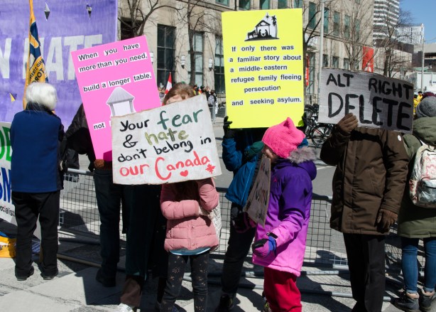a family, parents and children, hold 4 signs at a protest 