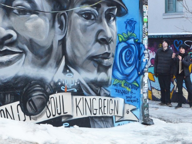 2 young men looking at street art in a lane, a large mural with two black and white mens faces in the foreground 