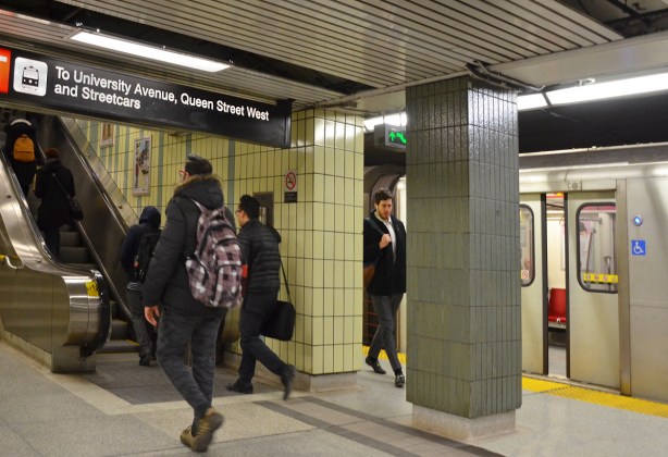 inside Osgoode subway station, at platform level, one subway is just closing its doors getting ready to leave, people are headed up the stairs. 