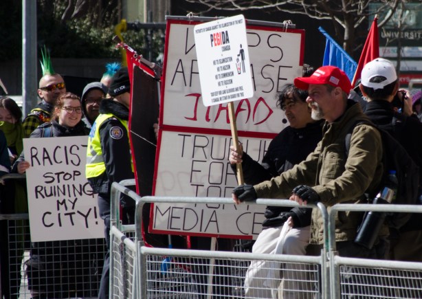 a man in a red MAGA baseball cap stands on one side of a metal barricade