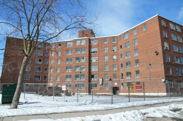 6 storey brick apartment building stands empty, a fence around it as it waits for demolition