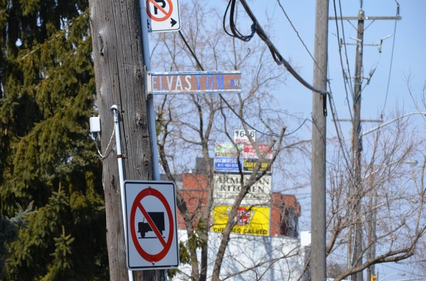 wooden pole with street sign for Elvaston and a no truck sign, in the background, signs from stores in a strip mall 