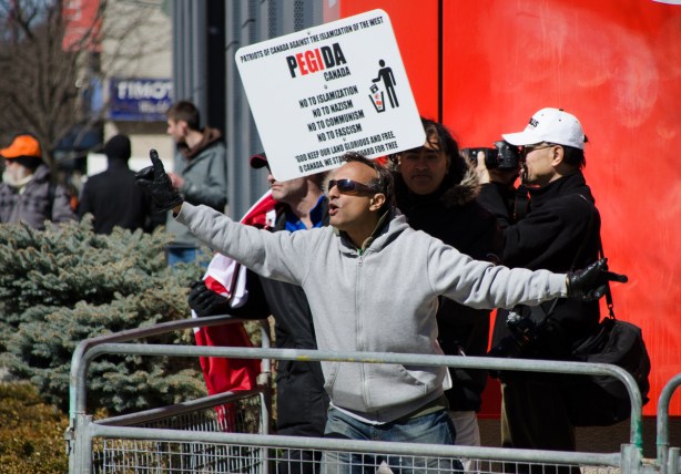 a brown skinned man in a grey sweatchirt mocks the crowd at a protest rally 
