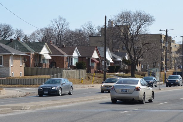 a few cars on the street driving past some small bungalows 