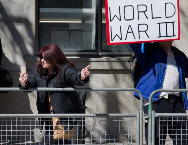 a woman with dyed auburn hair is making a video of herself at a protest on her cell phone 