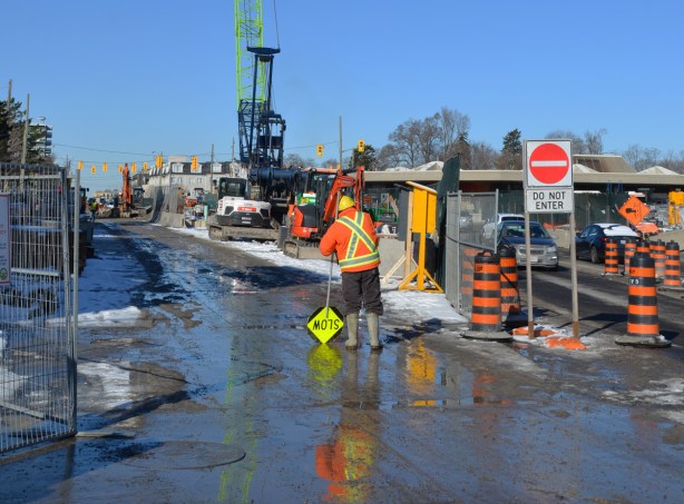 workman with a slow sign upside down, on a construction site in the middle of a street, crosstown eglinton lrt 