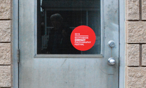 red circular sticker on a window, marking a gallery that is participating in contact photography festival 