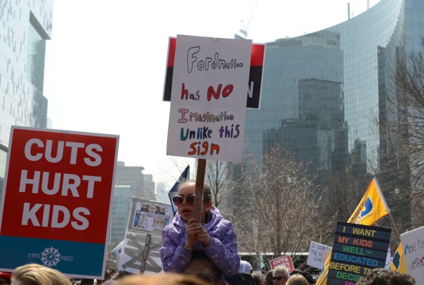 child on adult shoulders. person holding a placard protesting Doug Fords proposed cuts to education funding, 