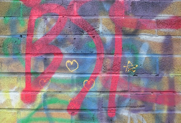 three tiny yellow hearts and a tiny yellow star drawn on a wall with colourful spray paint graffiti 