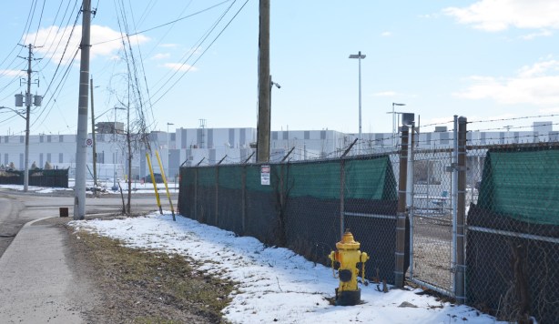 green construction fence in front of a long low building in two shades of grey