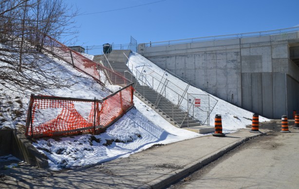 new concrete steps, still fenced off, up a hill with a light covering of snow to a new bridge