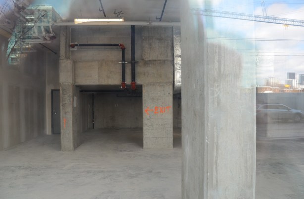 looking through the window of a building under construction, concrete walls, some black pipes, also in orange paint the word exit with an arrow 