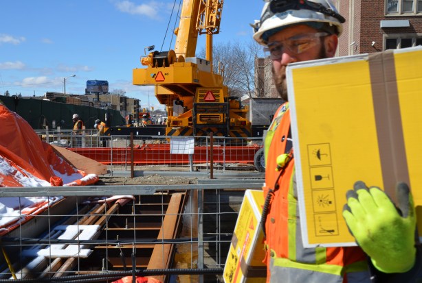 a workman in a hard hat and carrying yellow packages walks in front of the camera on a construction site