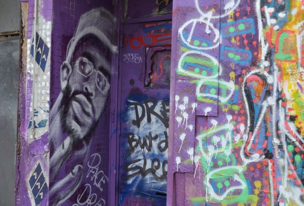 wall and doorway painted purple, a black man's face in greys on one side of the entranceway, other graffiti too