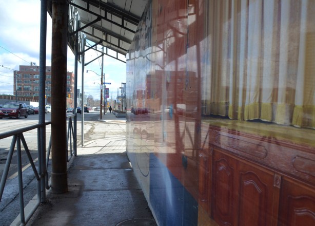 reflections in hoardings that are covered with a picture of yellow curtains and brown wood, sidewalk beside the hoardings and a wood structure over the sidewalk
