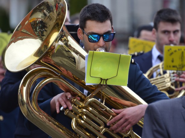 a young man plays a tuba in a marching band he is wearing bright blue sun glasses 