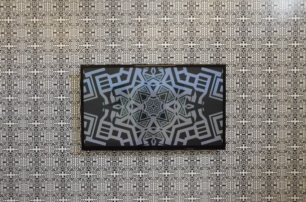 a wall covered with black and white pattern, a video monitor in the middle of a wall playing a video of more black and white patterns 