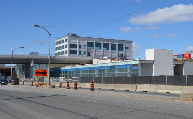 new building under construction, older white large building behind it. road in foregraound, Mt Dennis LRT station under construction 