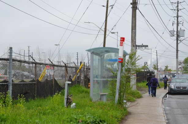 bus shelter at Bertal Rd near the new facility, barbed wire fence around the building, grass and weeds around the shelter
