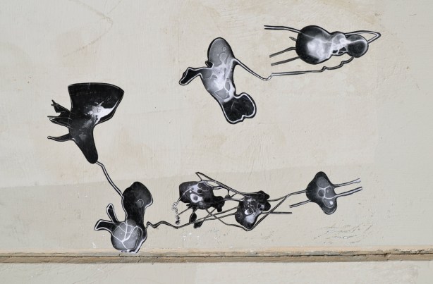 seven black and white photo paste ups that look like ameobas or primitive life forms on a concrete wall, outdoors, 