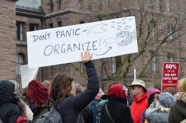 in the middle of a protest crowd, a woman holds up a sign that says Don't panic, organize 