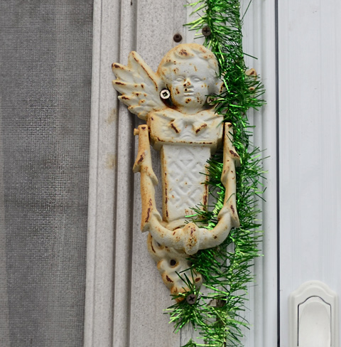 old rusty white door knocker with metallic green garland beside it 